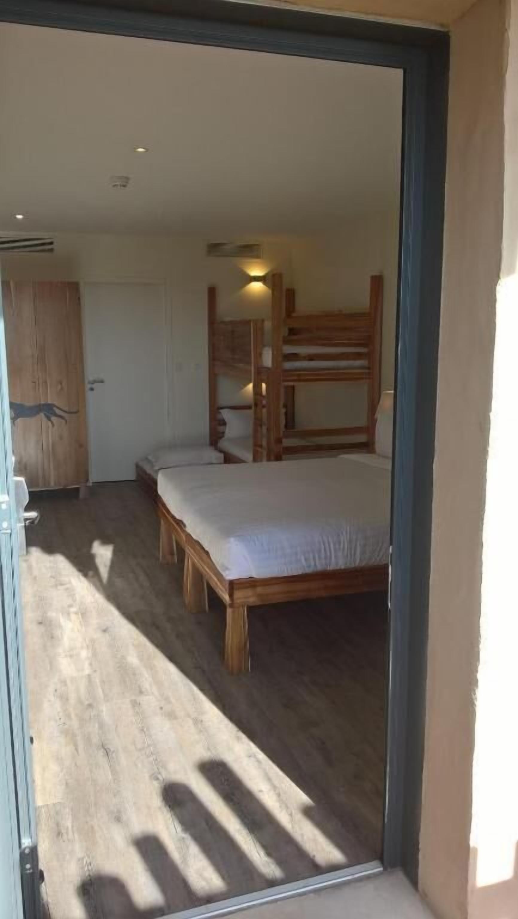 Un dormitorio con una cama litera y una cama individual, suelo de madera y un armario.