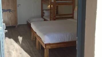 A bedroom with a bunk bed and a single bed, wooden flooring, and a wardrobe.