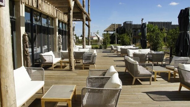 Un espacio de patio al aire libre con mobiliario de mimbre, una terraza de madera y una estatua de jirafa.