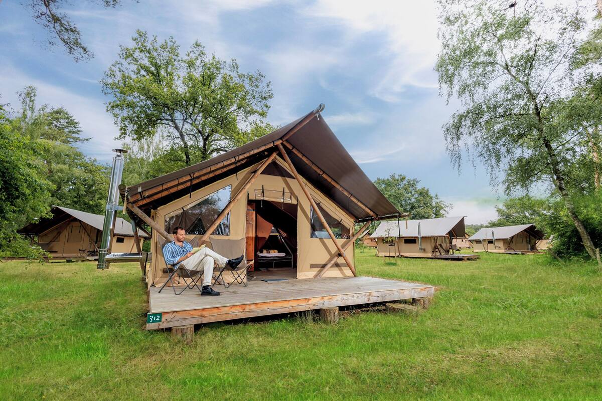 A tented accommodation with a wooden deck, a person seated, and another person standing.