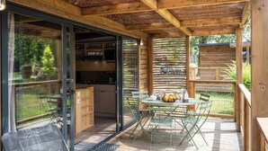 Een houten terras met een eettafel, een schuifdeur naar een keuken en uitzicht op de omgeving.