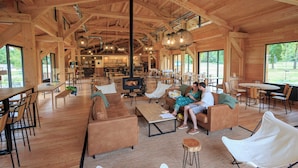 Ruim houten interieur met hoge plafonds, een centraal gelegen open haard en een combinatie van zithoeken met banken en stoelen.