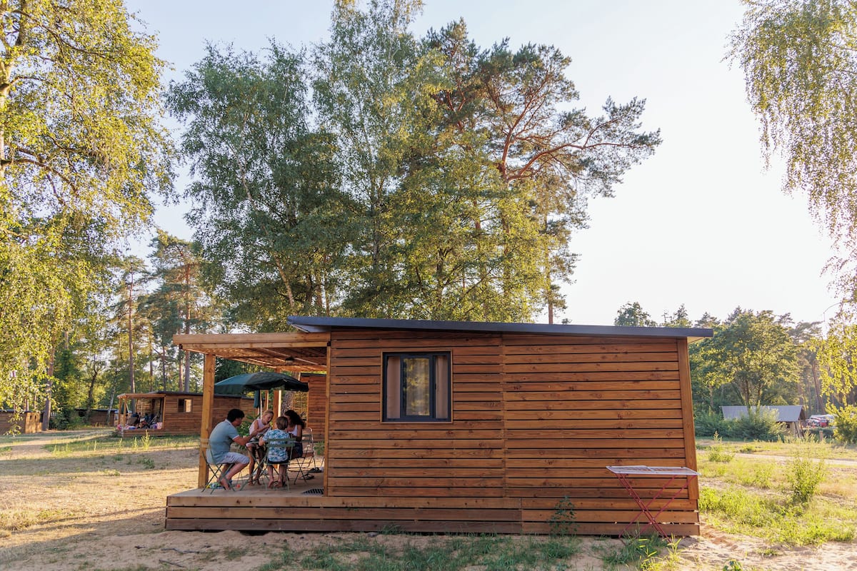 A wooden cabin with a small porch and a window, surrounded by trees.