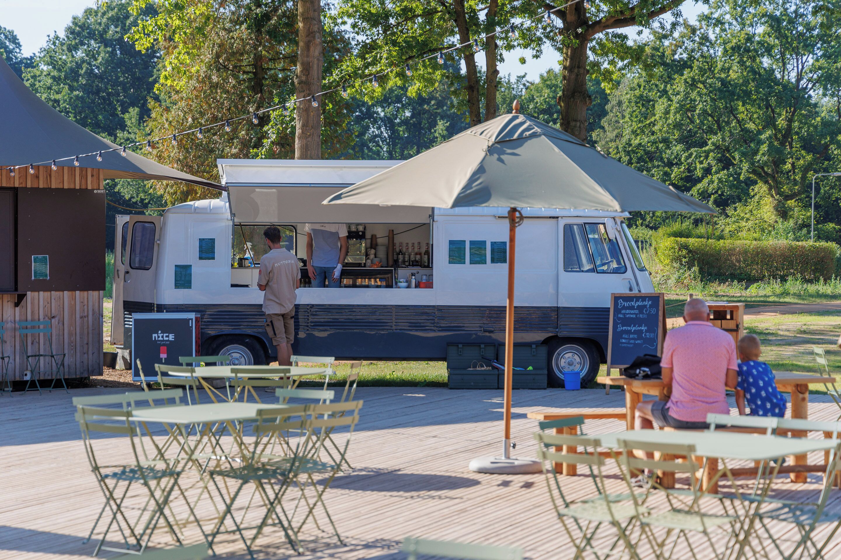 A food truck with a menu board, outdoor seating, and a shaded area.