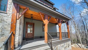 A stone house with a wooden porch, a stone entrance, and a balcony with a railing. - Modern Mountain Lodge with Great Amenities (Boone)
