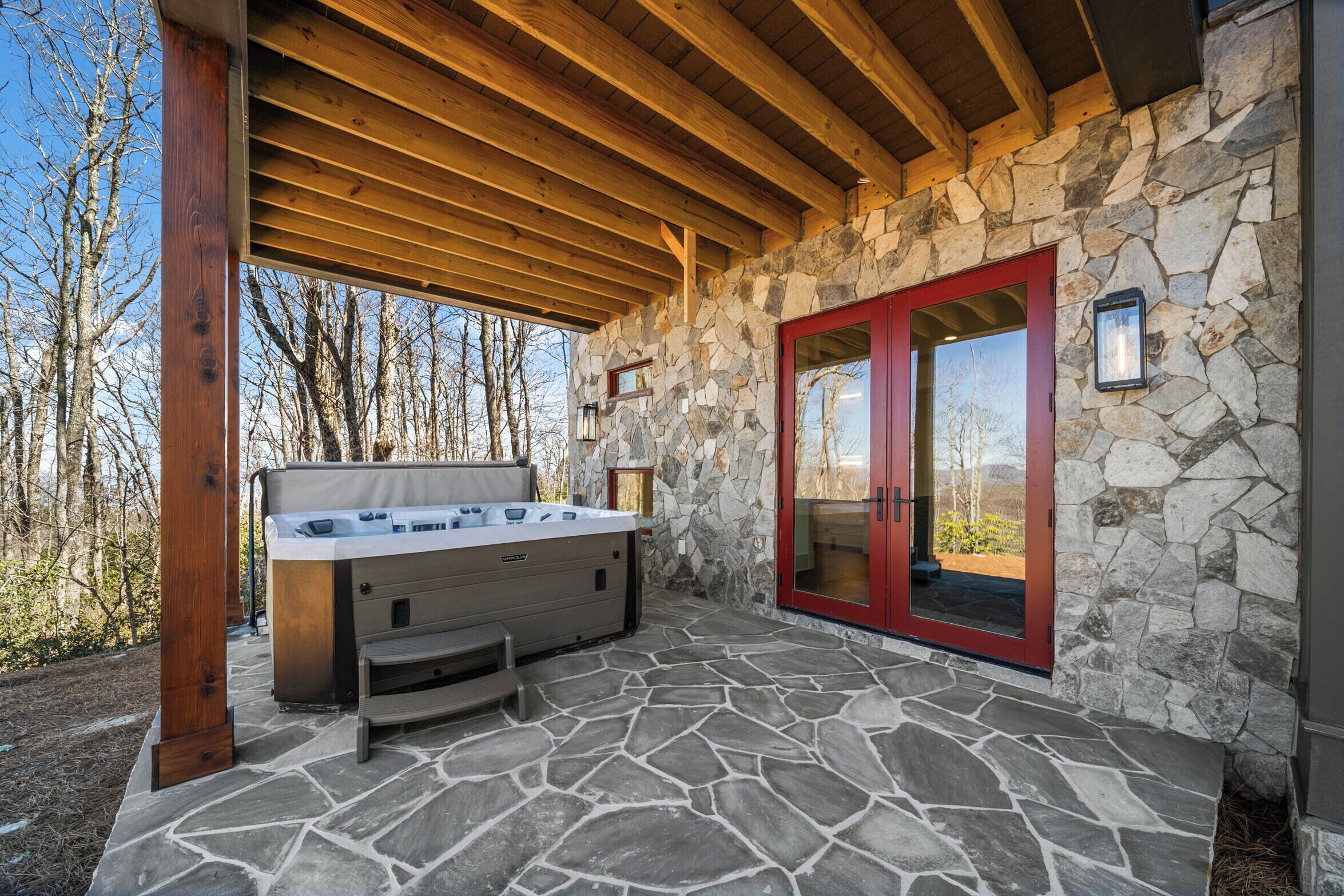 A stone patio with a hot tub, wooden beams, and a stone wall with a red door.