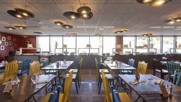 Un restaurante con varias mesas y sillas, piso de baldosas y techo con lámparas colgantes.
