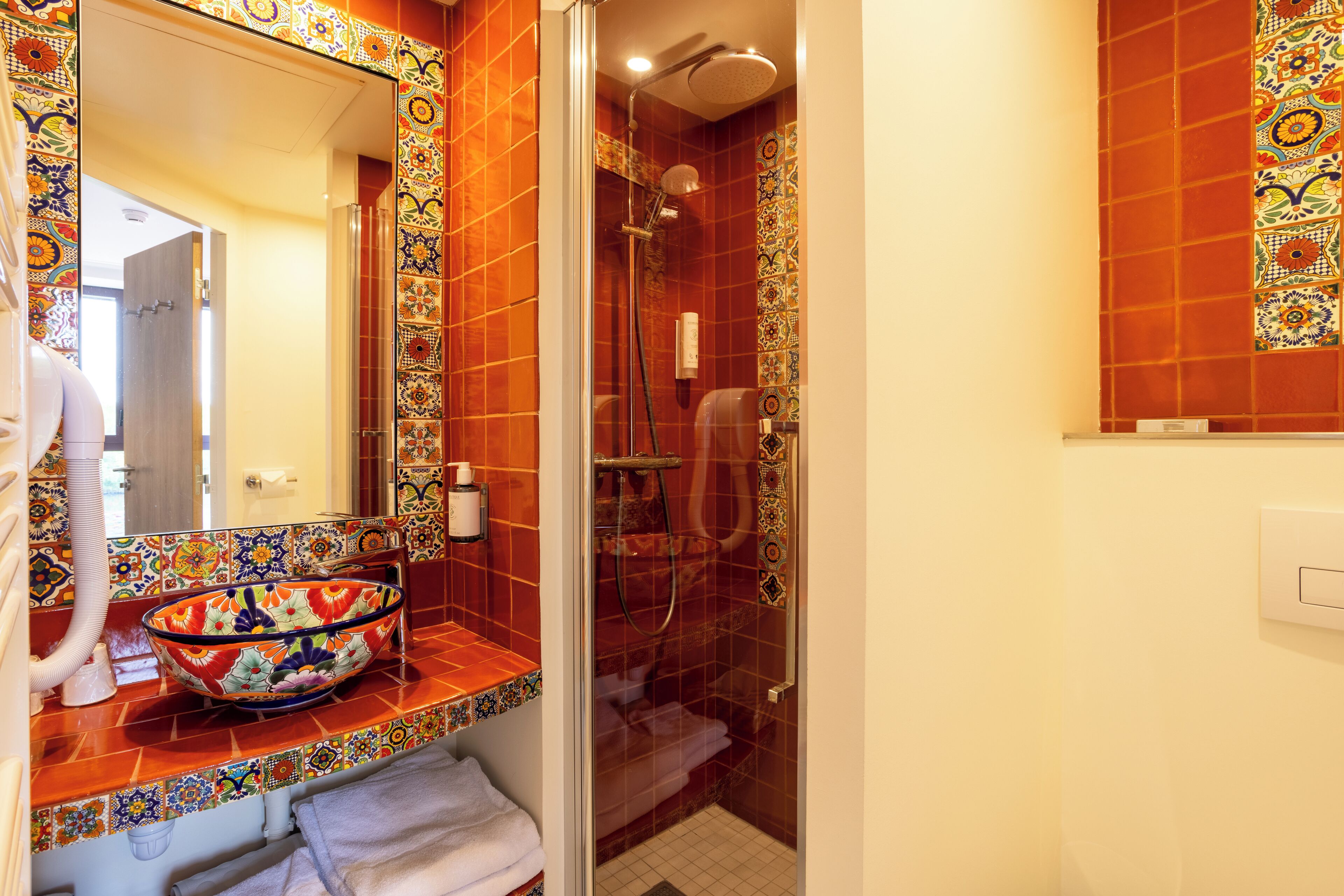 A bathroom with a tiled shower, a glass-enclosed sink, and a mirror.