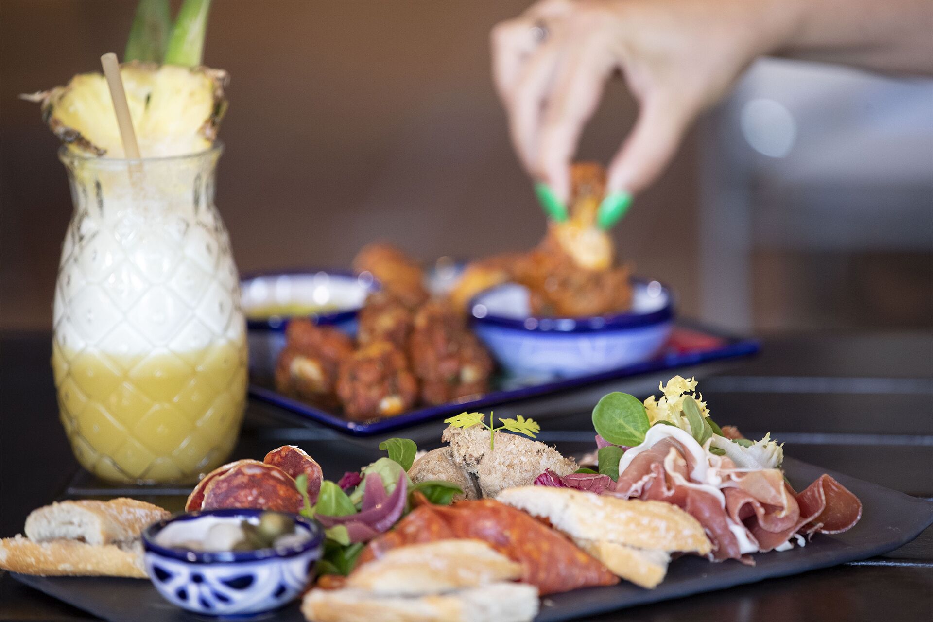 Variedad de aperitivos, incluyendo embutidos, pan y una bebida de piña, sobre una mesa.