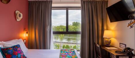A hotel room with a bed, a desk, a chair, a TV, and a window with curtains.