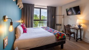 A hotel room with a bed, a desk, a chair, a TV, and a window with a view of greenery. - Les Rivages de Beauval (Saint-Aignan)