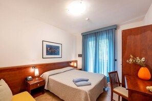 A hotel room with a bed, bedside table, lamp, chair, and a desk with a vase.