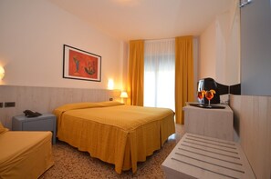 A hotel room with a double bed, a desk with a lamp, a phone, and a painting on the wall. - Hotel Olimpia - Family Suite Standard (Bibione)