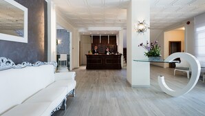 A modern hotel lobby with a reception desk, a white sofa, and a unique glass table with a large white letter 'G'.