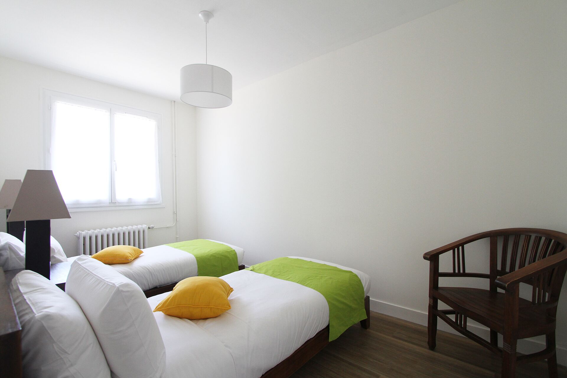 Un dormitorio con dos camas, una silla, una lámpara y una ventana.