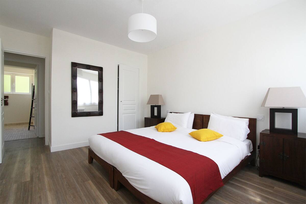 A hotel room with a large bed, two bedside tables with lamps, a mirror on the wall, and a door leading to another room.