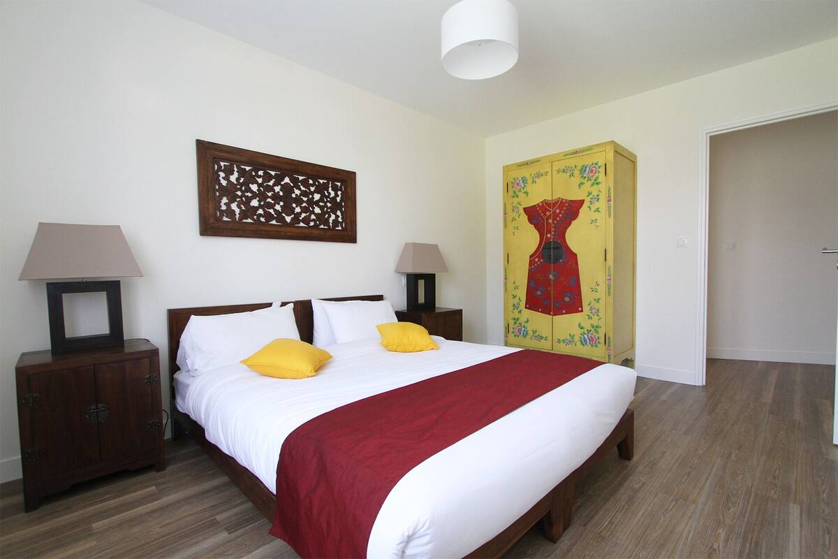 A bedroom with a wooden bed, two bedside tables with lamps, a decorative wall piece, and a wardrobe with a floral design.