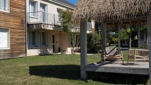 Un edificio de dos pisos con un balcón, una estructura de techo de paja y un patio cubierto de césped.