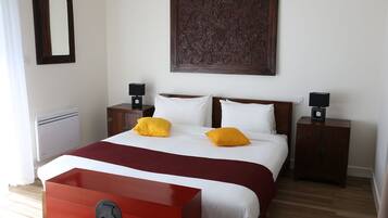 A hotel room with a bed, two bedside tables with lamps, a red cabinet, a large mirror, and a decorative wall panel.