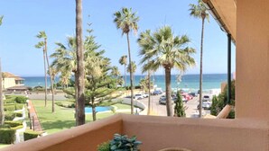 A balcony with a view of the ocean, palm trees, and a parking lot.