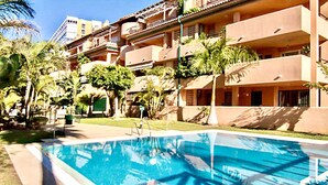 A hotel with a swimming pool, palm trees, and a multi-story building with balconies.