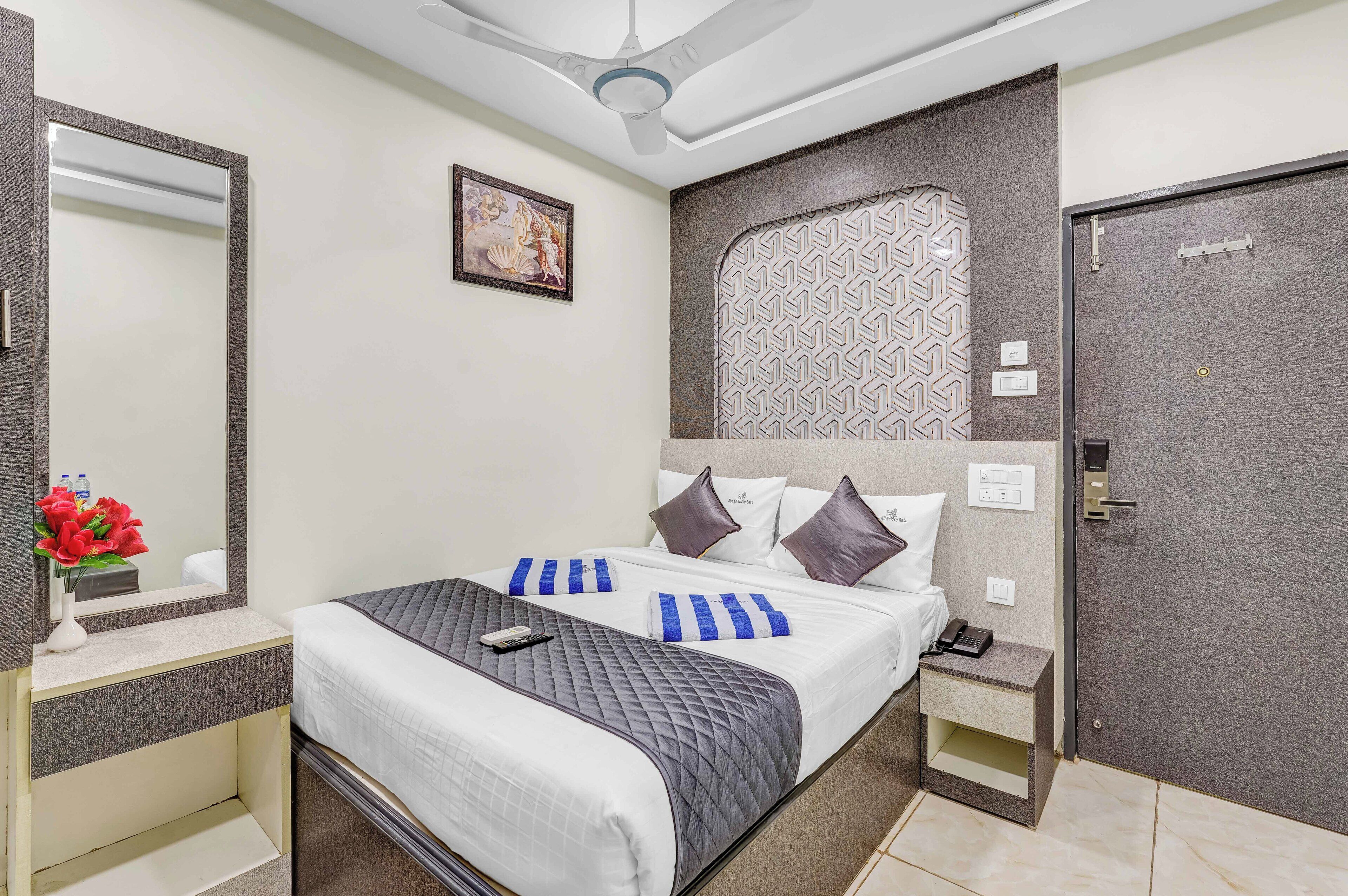 A hotel room with a bed, bedside tables, a mirror, a ceiling fan, a patterned wall, and a door.