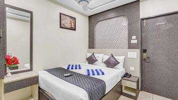 A hotel room with a bed, bedside tables, a mirror, a ceiling fan, a patterned wall, and a door.