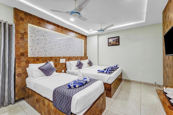 A hotel room with two beds, a wooden accent wall, a ceiling fan, and a flat-screen TV. - The K11 Golden Gate (Chennai)