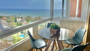 A balcony with a glass table and chairs, a wicker basket, and a view of the ocean and buildings. - Marbella - Beachside One bedroom apartment (Marbella)