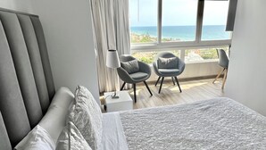A modern bedroom with a large bed, two armchairs, a nightstand, and a view of the ocean. - Marbella - Beachside One bedroom apartment (Marbella)