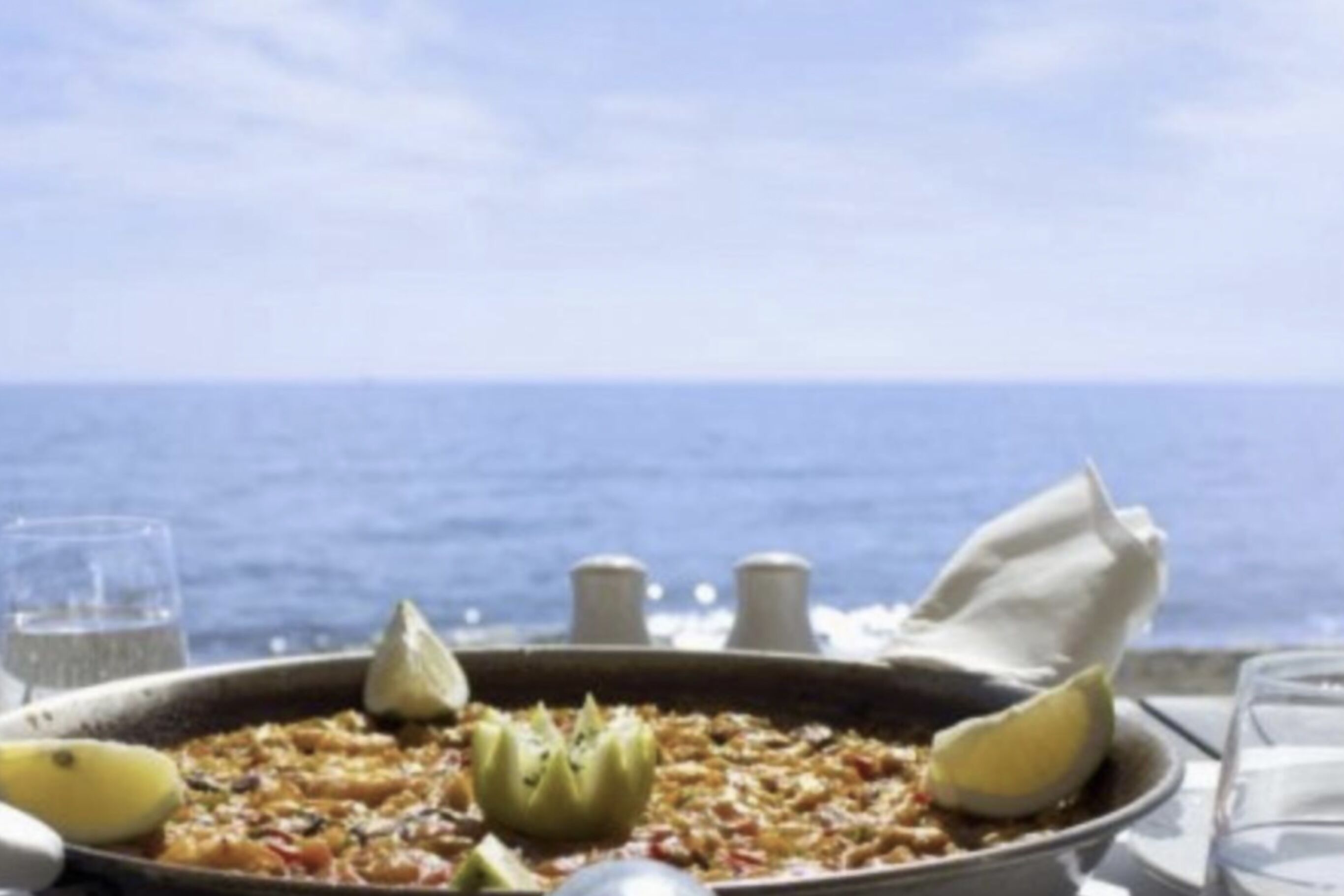 Un plat de fruits de mer est servi sur une table, avec vue sur la mer.