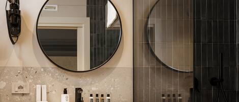 A modern bathroom with a round mirror, a sink with toiletries, and a glass-enclosed shower.