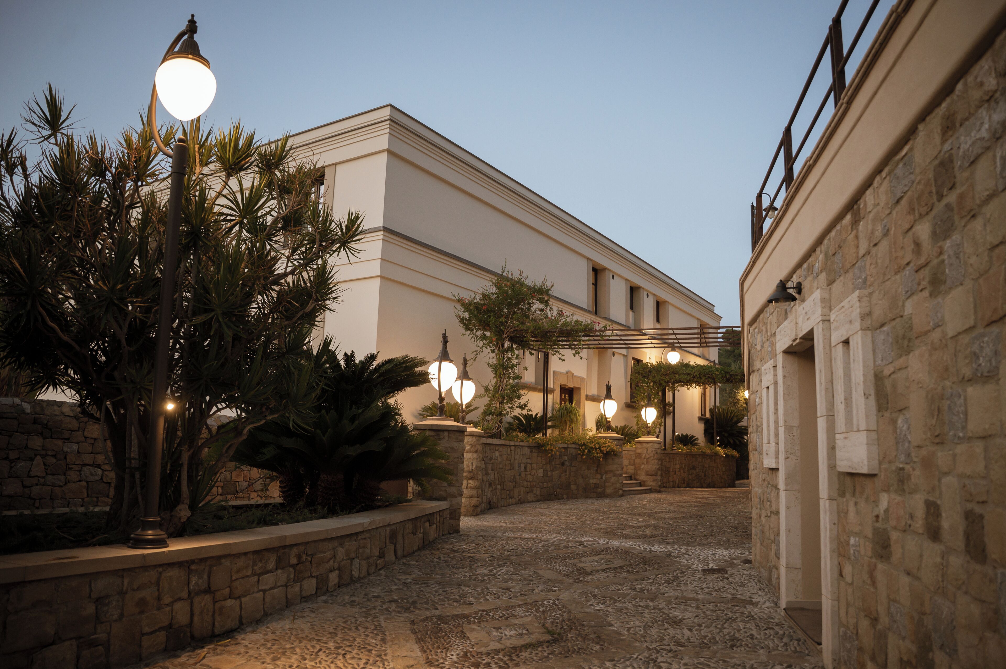 A courtyard with a stone pathway, a lamp post, and a building with a lighted entrance.