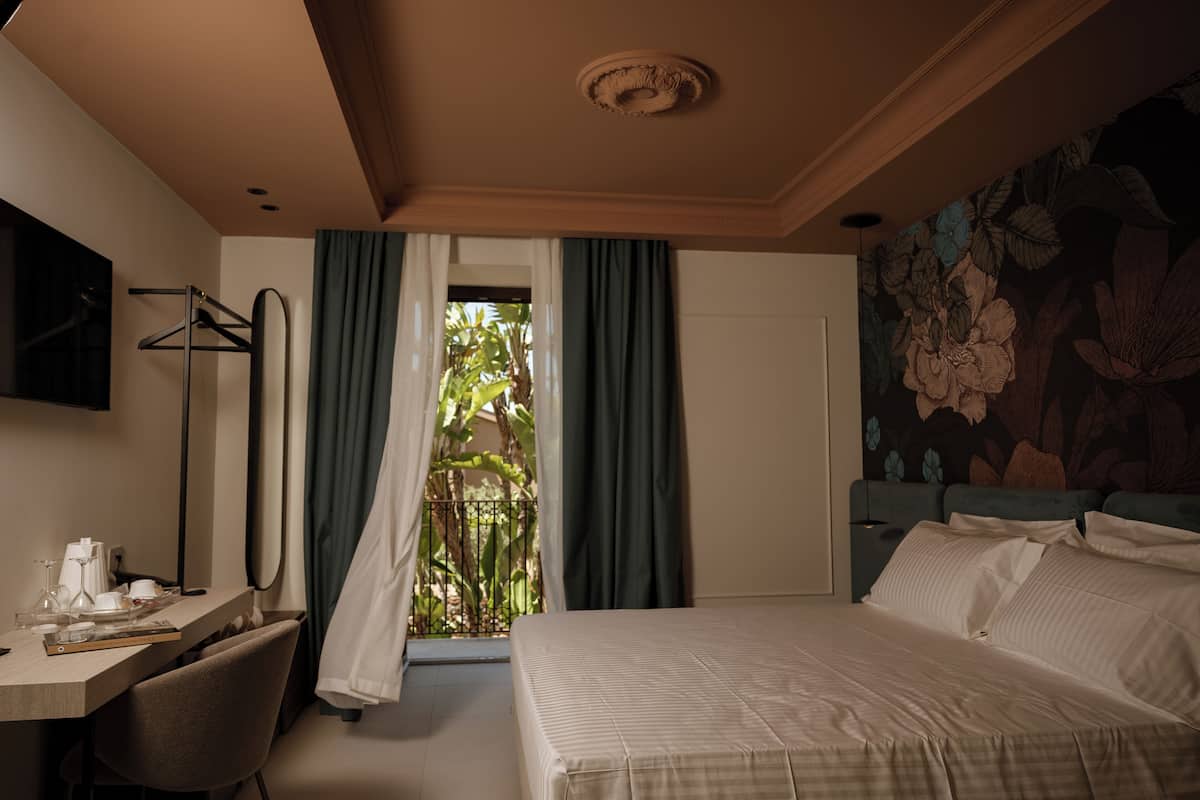 Una habitación de hotel con cama, escritorio, silla, televisor y ventana con cortinas.