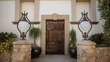 Dos puertas dobles con diseños intrincados, flanqueadas por dos macetas grandes y dos farolas ornamentales.