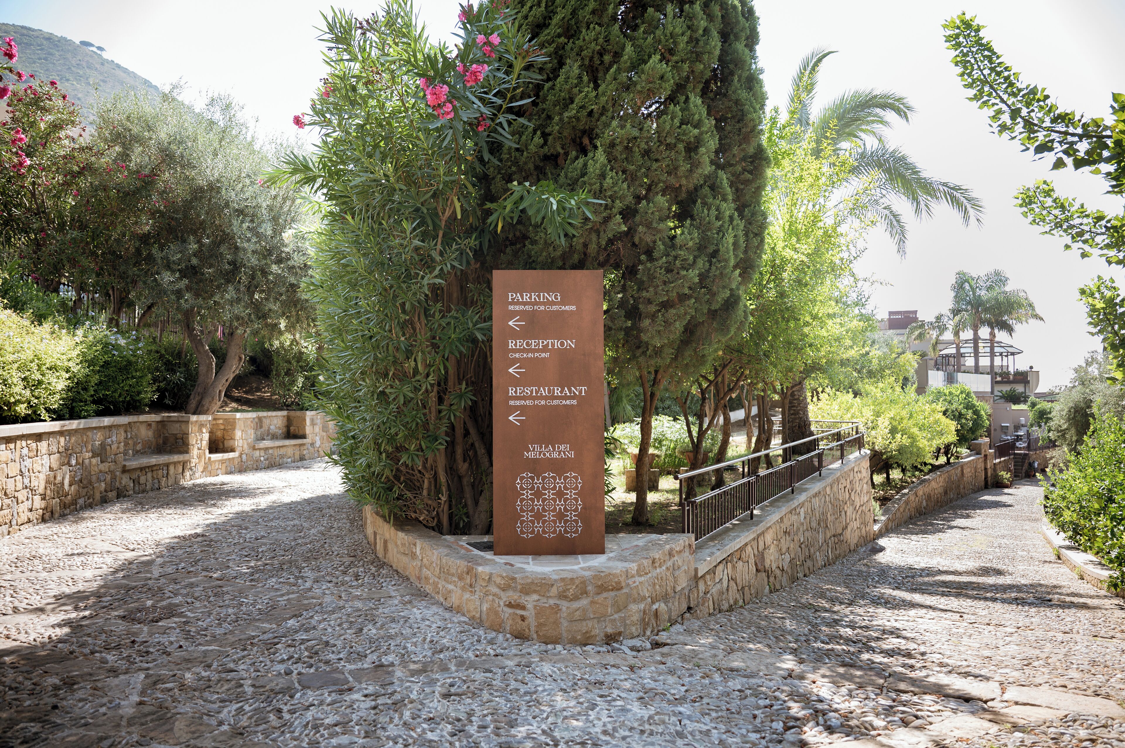 A stone pathway leading to a signpost with directions to parking, reception, and a restaurant.