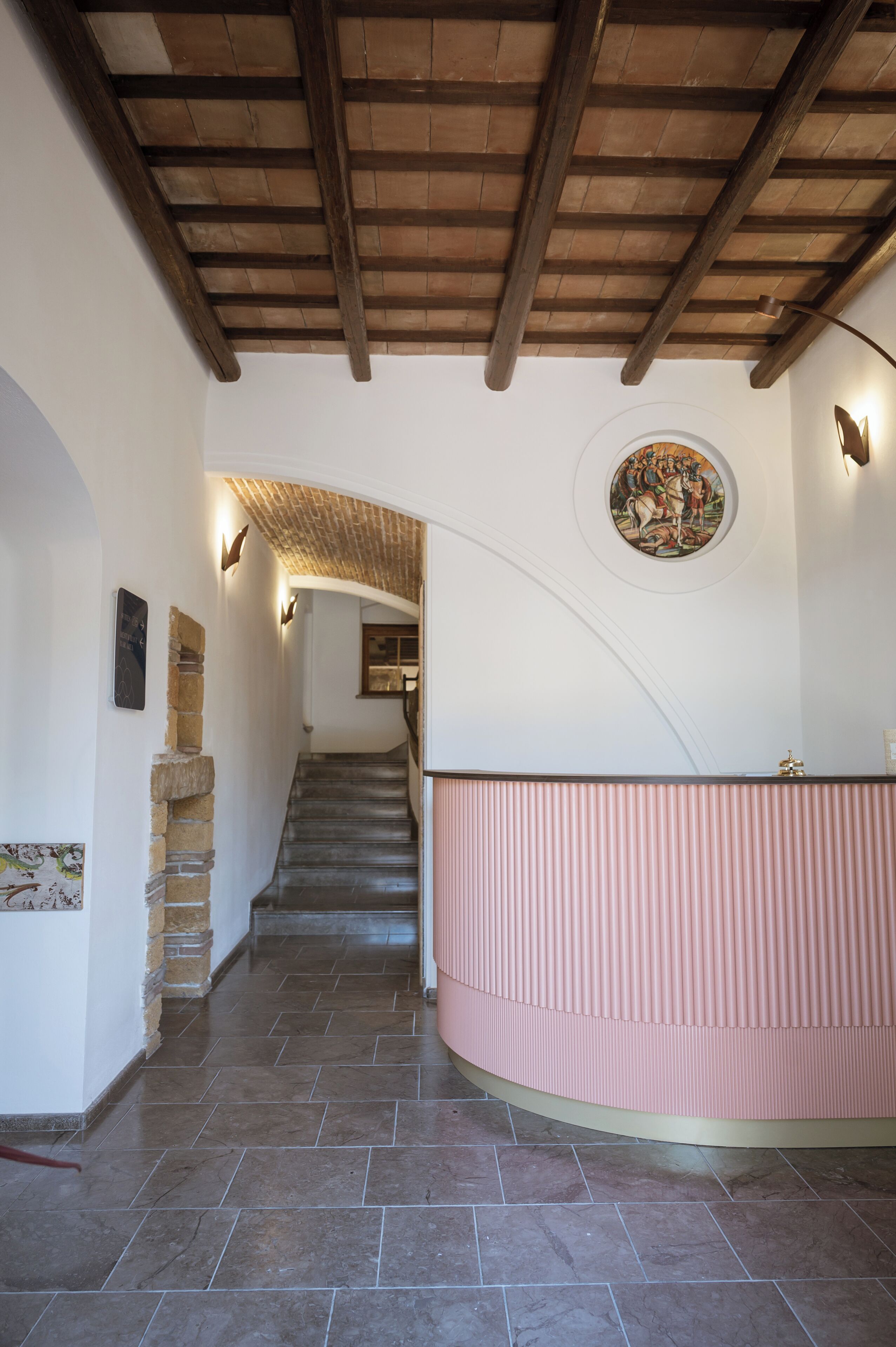 A curved staircase with a stone wall on the left and a pink railing on the right.