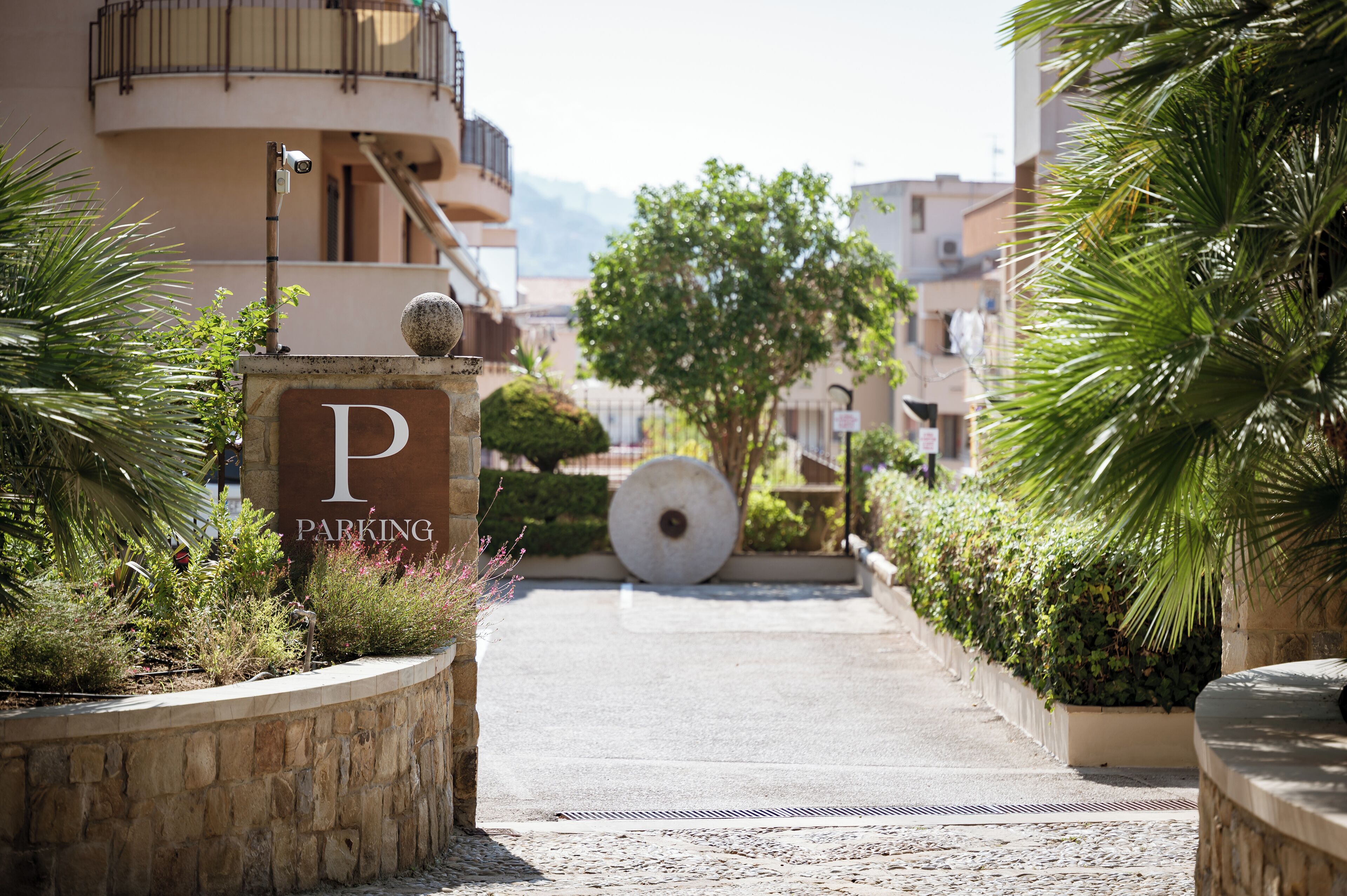 A pathway leading to a building with a 'PARKING' sign, surrounded by greenery and a stone wall.