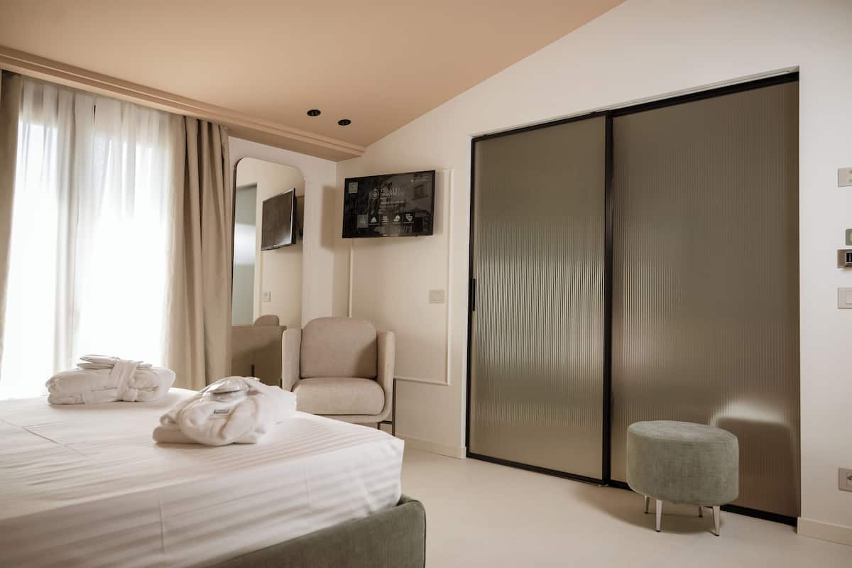 Una habitación de hotel con una cama, una silla, un pequeño reposapiés, una puerta corredera y un televisor montado en la pared.