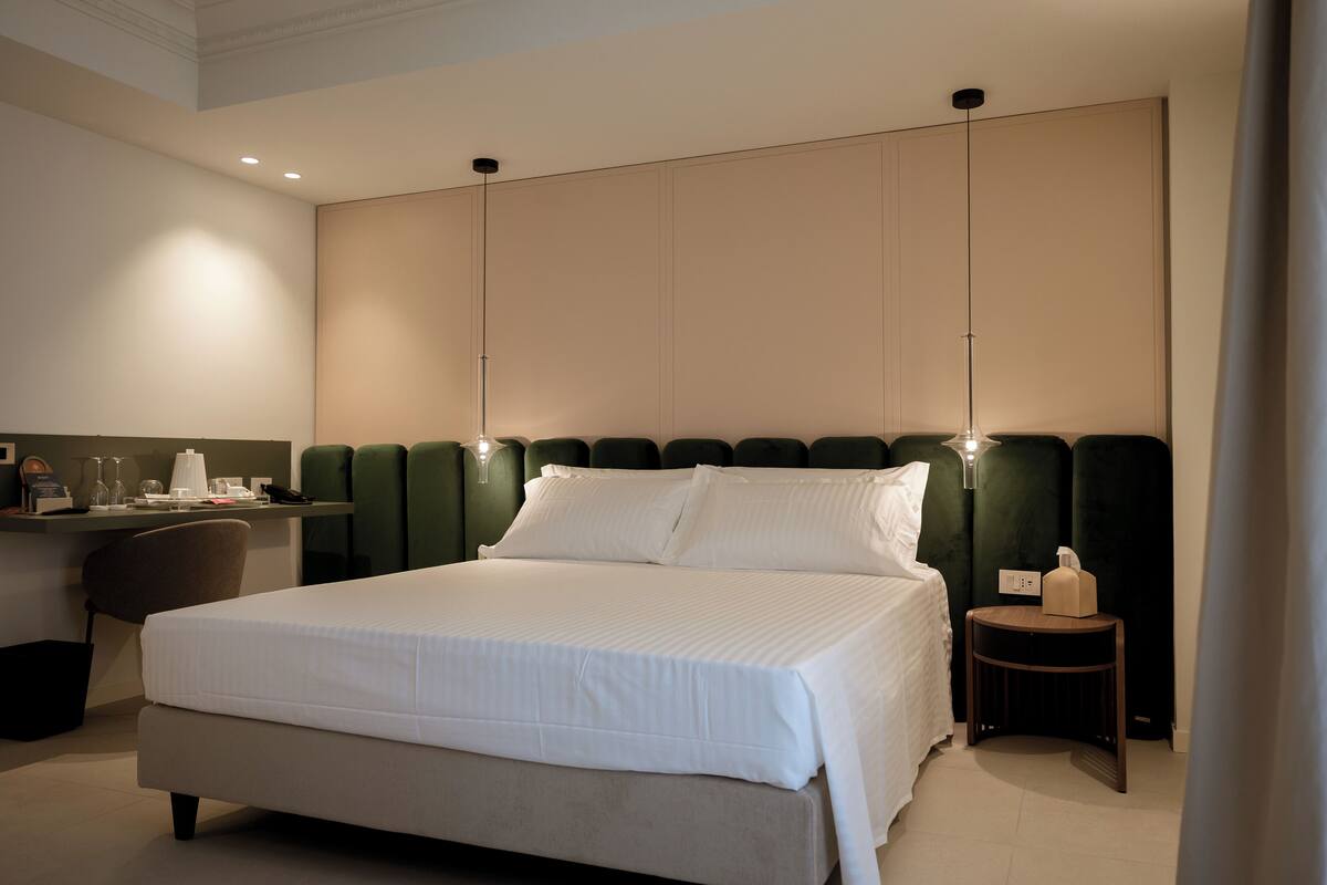 Habitación de hotel con una cama grande, un escritorio con silla, una mesita pequeña y una mesita de noche.