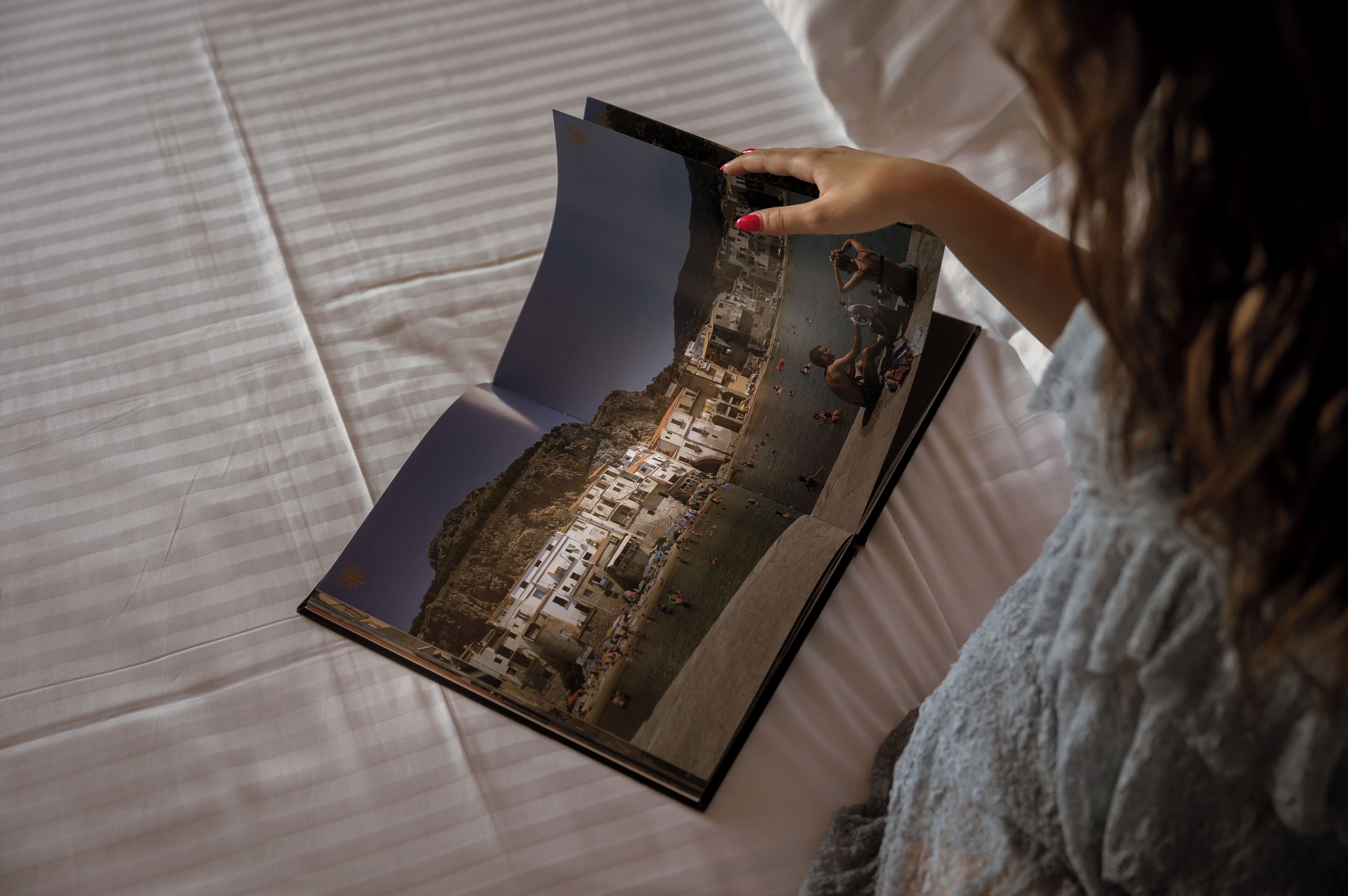 Une personne tenant un livre ouvert, sur lequel figure une photographie d’une ville côtière.