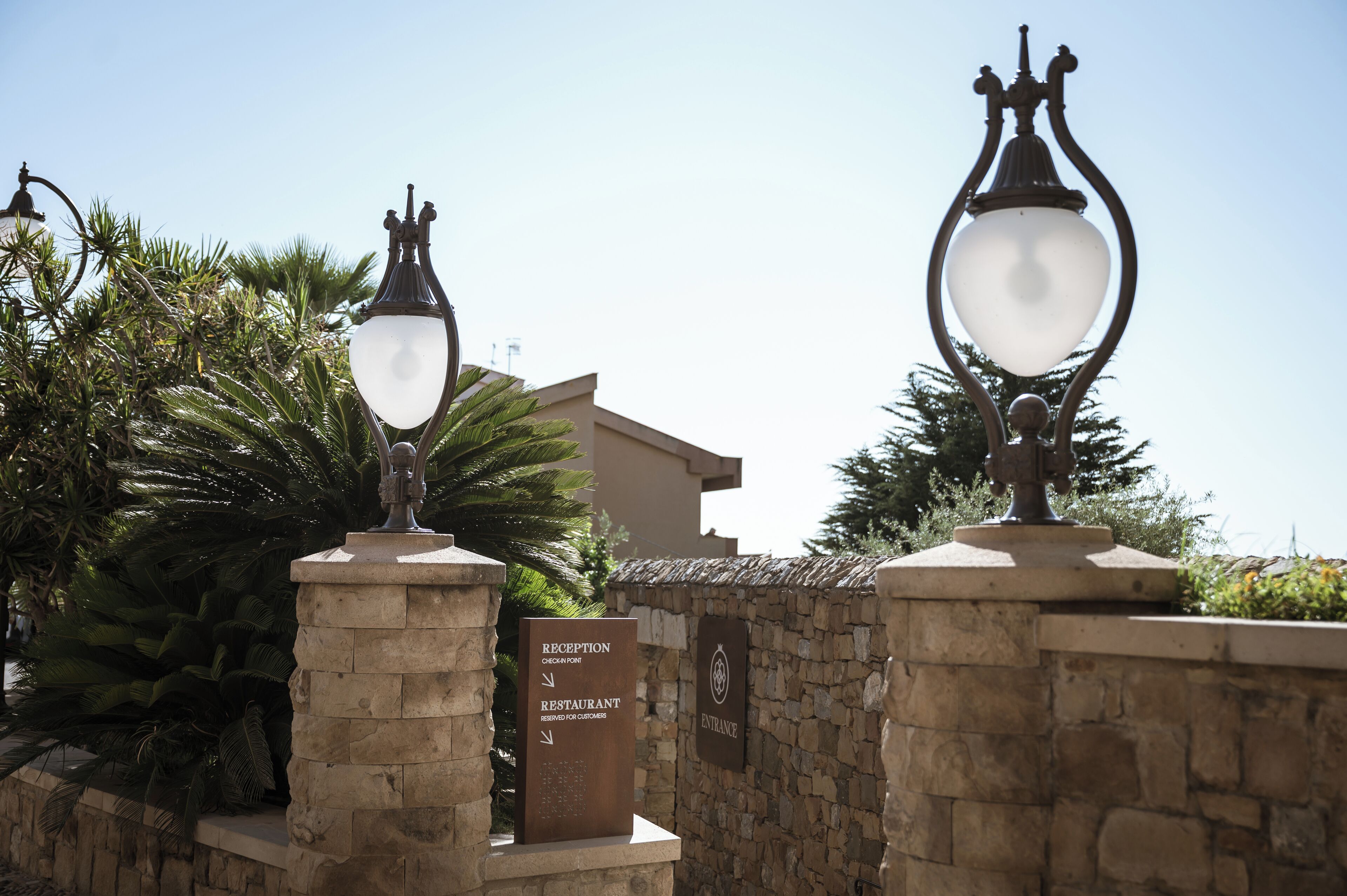 Señal de recepción con indicaciones hacia el restaurante y la entrada, frente a una pared de piedra con farolas decorativas.