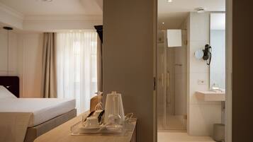 Une chambre d’hôtel avec un lit, une table de chevet sur laquelle se trouve un plateau avec des articles pour le petit-déjeuner, un verre d’eau et un espace douche doté d’une porte en verre.