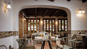 Comedor con mesas dispuestas para comidas, vigas de madera en el techo y amplias ventanas que dejan entrar luz natural.