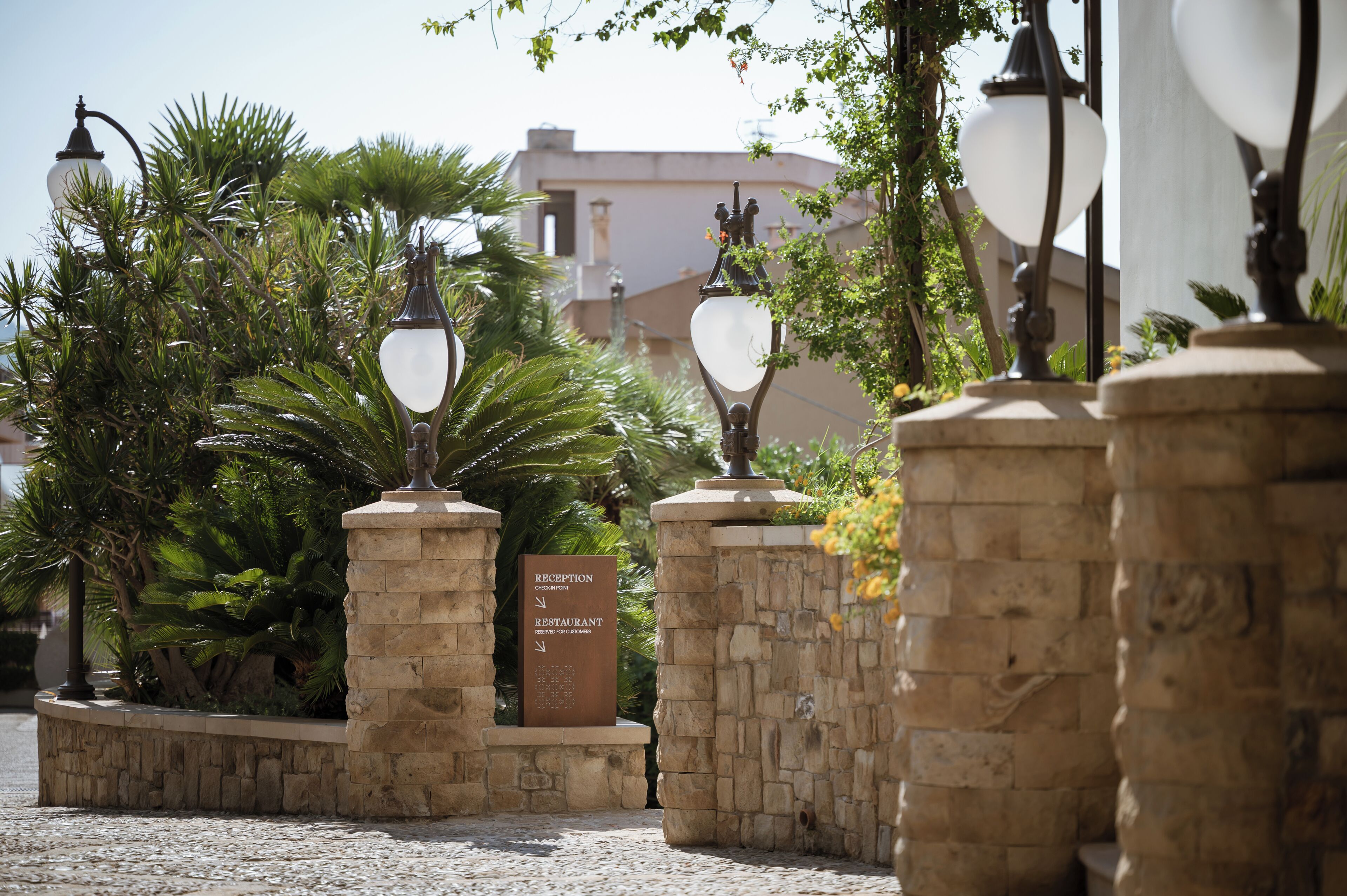 Un espace d’accueil avec une enseigne indiquant la présence d’un restaurant, entouré de piliers en pierre et de lampadaires décoratifs.