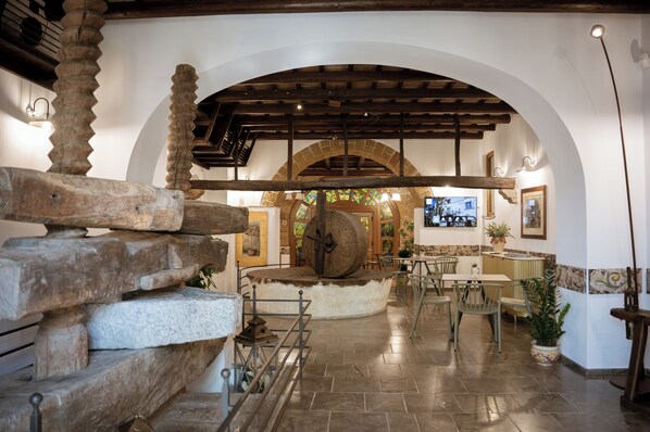 A stone spiral staircase, a large stone mill, and a seating area with tables and chairs in a rustic interior.