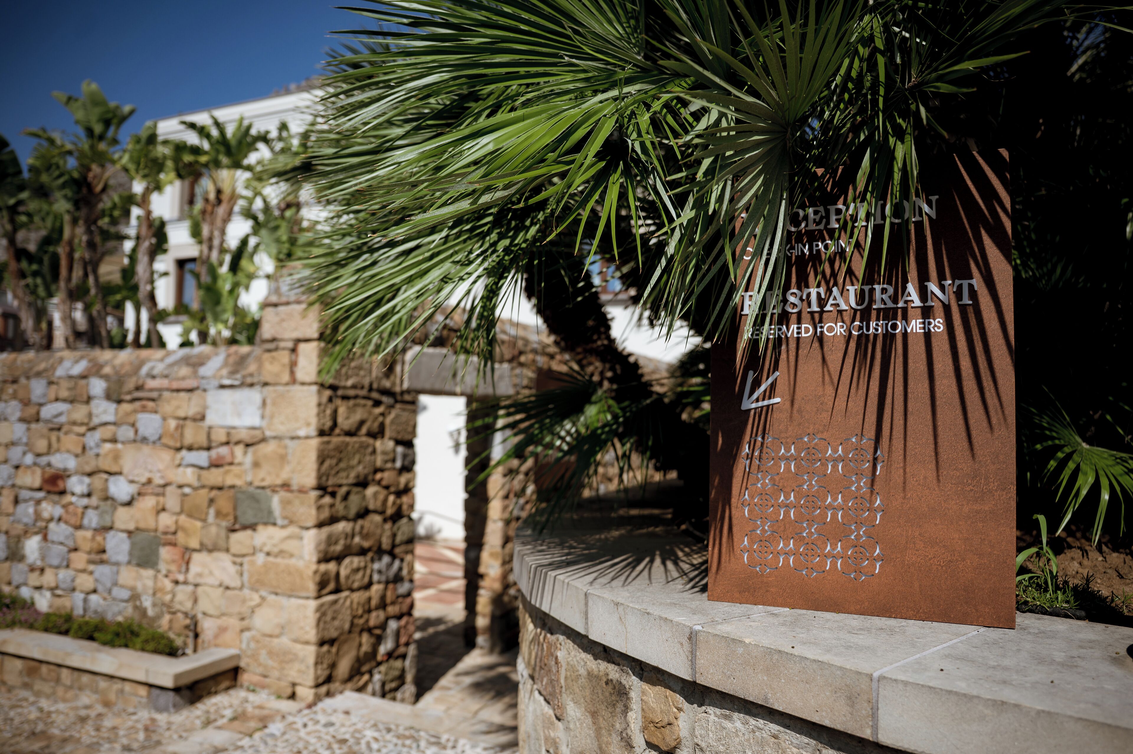 A reception sign for a restaurant with a stone wall and palm trees in the background.
