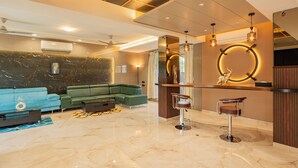 A modern living room with a sectional sofa, a bar area with stools, and a marble floor. - Alaya Stays - Imperial Calista 4BHK near Khandala Hills (Lonavala)