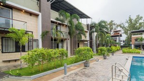 A modern building with a swimming pool, surrounded by well-maintained greenery and a paved walkway. - Alaya Stays - Imperial Calista 4BHK near Khandala Hills (Lonavala)