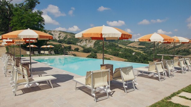 Zona de piscina con sillones reclinables y sombrillas, rodeada por un paisaje montañoso.